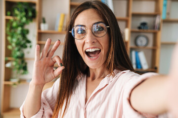 Image of businesswoman gesturing ok sign while taking selfie photo