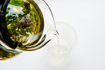 Close up of  green tea being poured from teapot into transparent glass