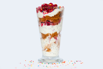 Sweet dessert from biscuits berries and yogurt in transparent tall glass, isolated on white background.