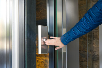 Woman pressing the button of the modern elevator made from glass.