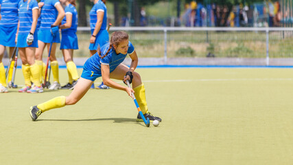 Young field hockey female player hitting the ball