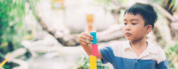 Asian young boy playing wooden block toy on table for creative and development, happy child learn skill for activity puzzle and creativity for game at home, education concept, banner website.