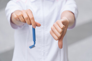 Close up womens hands hold a razor. Thumb down with indignation reveals doctor
