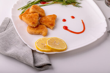 On the table on a white plate, chicken nuggets with lemon.