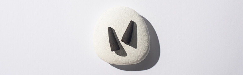 top view of black incense cones on spa stone on white background, panoramic shot