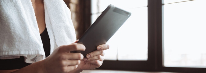 Lady with towel sitting in gym while using tablet