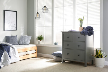 Grey chest of drawers near window in stylish bedroom interior