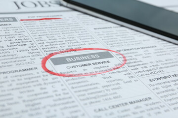 Obraz premium Newspaper with marked advertisement and smartphone. Job search concept