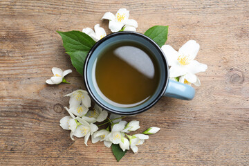 Cup of tea and fresh jasmine flowers on wooden table, flat lay