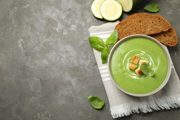 Tasty homemade zucchini cream soup served on grey table, flat lay. Space for text