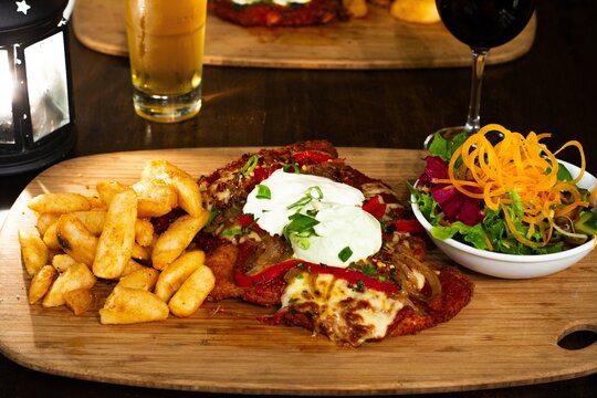 Chicken Parma With Chips And Salad On A Wooden Plate With Beer And Wine