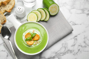 Tasty homemade zucchini cream soup served on marble table, flat lay