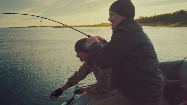 Friends fishing. Two amateur anglers fishing from the boat and fighting with trophy fish. Fishing rod bends under the big fish