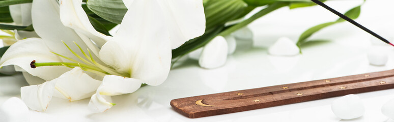 aroma stick on wooden stand near lily on white background, panoramic shot