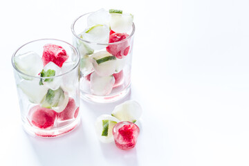 Cocktail glasses with berries in ice cubes on white table copy space