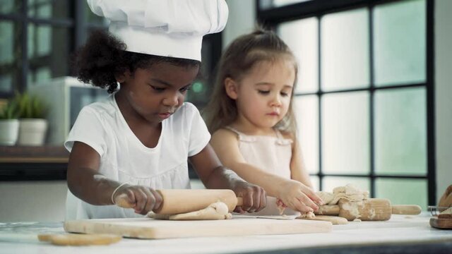 Diverse group of African American and Caucasian girls prepare the dough and bake cookies in the kitchen while learning in the class at school.