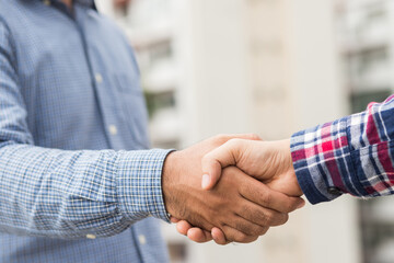 Naklejka na ściany i meble Two men shaking hands to dealing success agreement business. Business people wearing scott shirt on city view background.