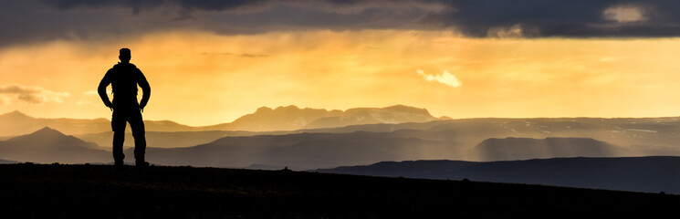 Hiking Man Silhouette enjoying amazing colorful sunset mountains. Fantastic panorama of misty and foggy layered mountains with dramatic clouds. Icelandic highland landscape. Iceland.