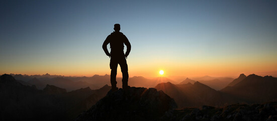 Man Silhouette reaching summit enjoying freedom and looking towards mountains sunset. Allgau Alps,...