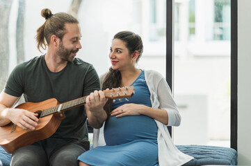 The man played the guitar for his wife to listen. She is pregnant They were all together in the house on the sofa. Family couple concept.