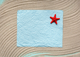 Fototapeta na wymiar Blank sheet of paper with red starfish on light sea sand. Texture of light sand. Flat lay, top view, copy space.