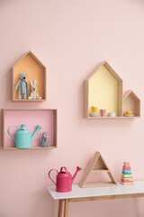 Fototapeta na wymiar Stylish house shaped shelves with toys and wooden table indoors. Baby room interior design