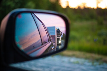 reflection in a side mirror of a distant mode of transport going along the highway at sunset