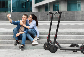 Friends using motorized kick scooters, taking selfies