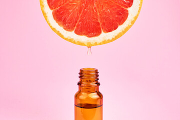 Citrus oil drop dripping from grapefruit slice into dark glass bottle