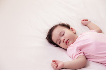 Adorable innocent baby girl sleeping on bed with good dream. Cute mixed race infant baby feel comfortable and taking a rest, relaxed and peaceful. Lovely toddler girl wear pink baby dress. copy space