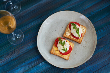 Large gray ceramic plate with toast and poached eggs, greens, tomatoes, sauce. Tasty breakfast. Glasses of wine.