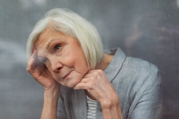 lonely senior woman loooking away while standing by window