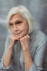 sad senior woman looking away through window glass