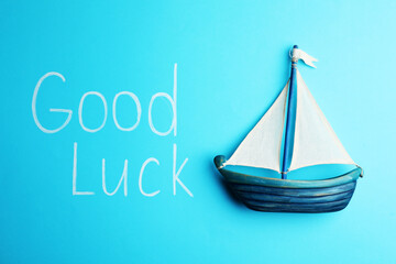 Phrase GOOD LUCK and boat on light blue background, top view