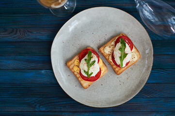 Large gray ceramic plate with toast and poached eggs, greens, tomatoes, sauce. Tasty breakfast. Glasses of wine.