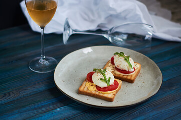 Large gray ceramic plate with toast and poached eggs, greens, tomatoes, sauce. Tasty breakfast. Glasses of wine.