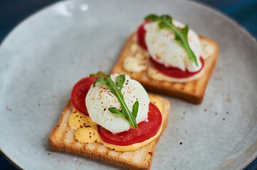 Tasty home breakfast of square toast with sliced fresh tomato and egg benedict with urugula.