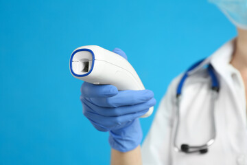 Doctor holding non contact infrared thermometer against light blue background, focus on hand....