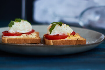 Large gray ceramic plate with toast and poached eggs, greens, tomatoes, sauce. Tasty breakfast. Glasses of wine.