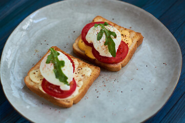 Tasty home breakfast of square toast with sliced fresh tomato and egg benedict with urugula.