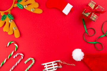 Christmas composition. Gifts, candy canes, headband antlers, santa hat, sleigh, Christmas sock on red background. Concept of winter holidays, new year, Christmas. Top view. Copy space