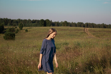 Naklejka na ściany i meble Beautyful woman walking outdoors. Fashion elegant lady in blue dress on nature