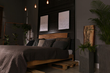 Comfortable bedroom with green plants and pictures on wall. Interior design