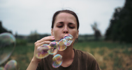 The girl blows soap bubbles. A young woman sits in nature and blows soap balls. The person in front.
