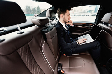 Young businessman talking on phone in car using his pc
