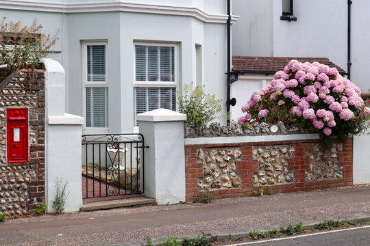 English coastal summer garden, with red letter box and hydrangeas and a sea pebble wall