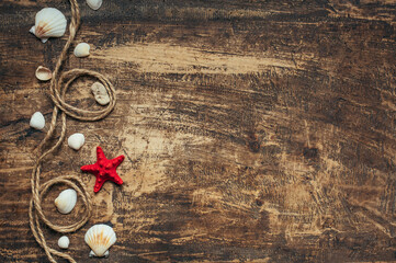 Fototapeta na wymiar Summer time, sea vacation. Red starfish, rope and seashells on dark wooden with place for text.