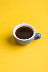 Small blue cup with black coffee at yellow minimal background