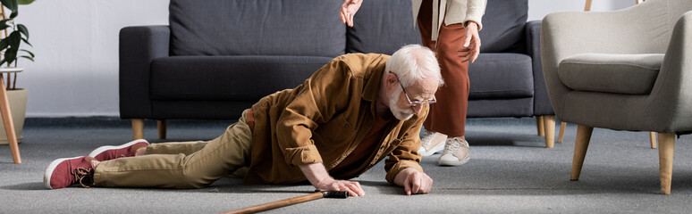 partial view of woman helping fallen senior husband to get up from floor, horizontal concept