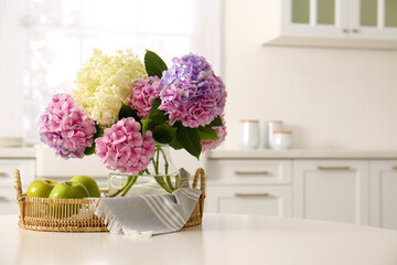 Obraz na płótnie Canvas Bouquet of beautiful hydrangea flowers and apples on table in kitchen, space for text. Interior design